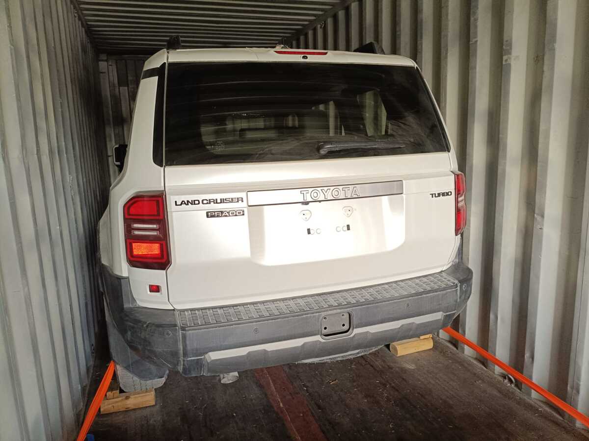 Toyota Prado w kontenerze z pasami mocującymi i klinami pod kołami.