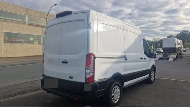 A van at a yard, with a car transporter in the background.